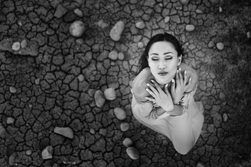 Black-and-white photo of the model on the background of stones and cracked soil