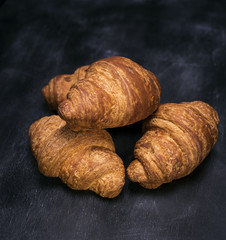 three baked croissants on a black background