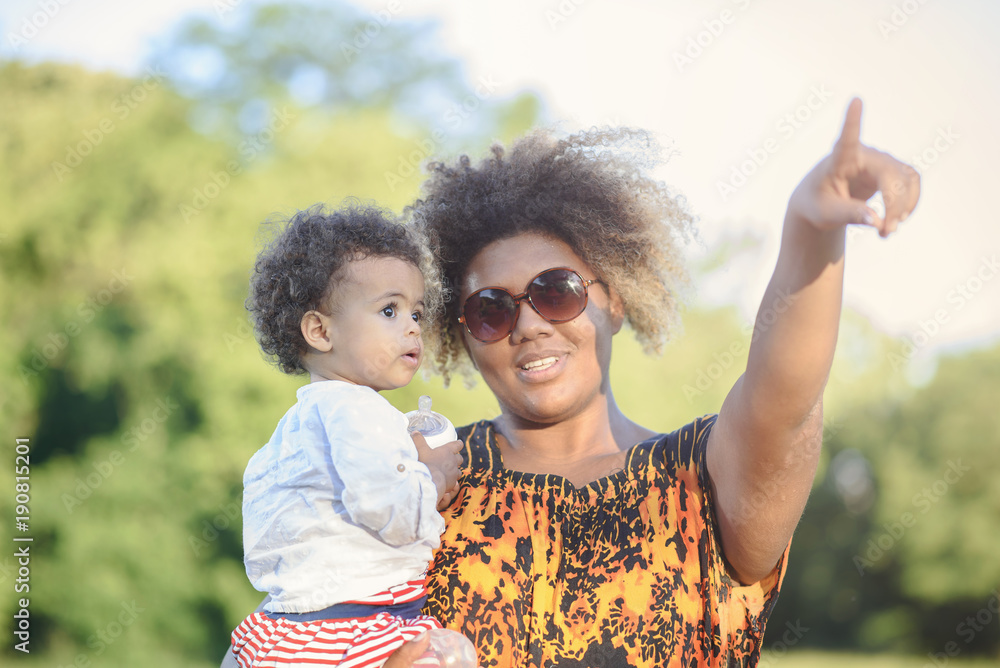 Poster Mother and daughter, african american and mixed race, playing together in a park, mom showing her daughter something in the sky