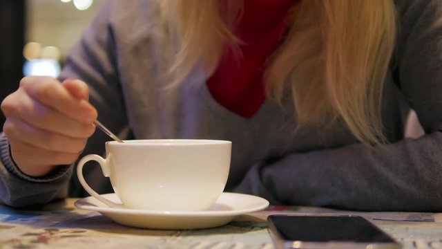 4k Pretty Blondie girl drinks tea from white cup and take spoon in cafe close-up  