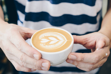 Cropped shot view of Barista holding a cup of latte coffee with his hands.