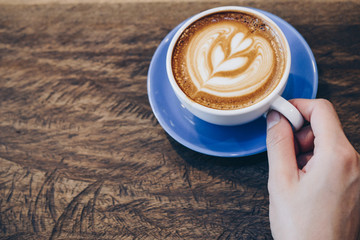 Cropped shot view of human hand with a cup of hot coffee latte.