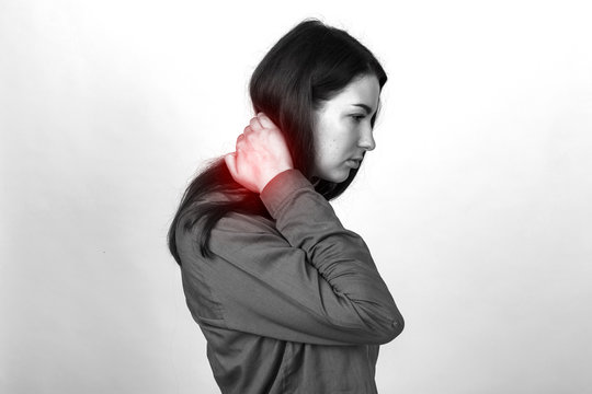 Portrait of a pretty woman holding her neck in pain and discomfort  standing over gray background. Black and white with a red accent