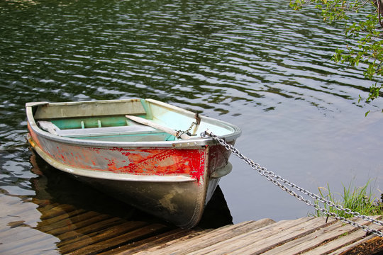 An Aluminum Row Boat Chained To The Shore By A Dock