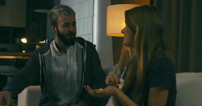 Young adult Caucasian couple sit on couch at home, watching TV, throwing popcorn at each other. 4K UHD