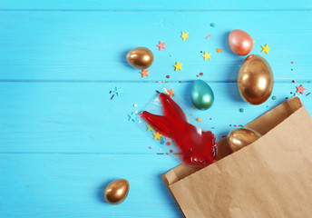 Paper package with bunny shaped lollipop and Easter eggs on wooden background