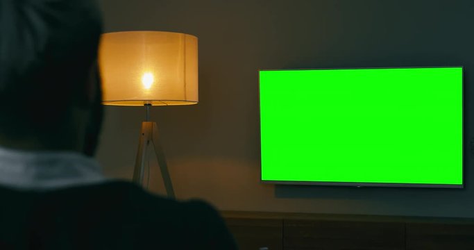 GREEN SCREEN Back view of Caucasian male sitting on sofa, watching sport basketball game on a TV screen. 4K UHD