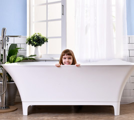Obraz na płótnie Canvas Happy little baby girl sitting in bath tub playing with duck toys in the bathroom