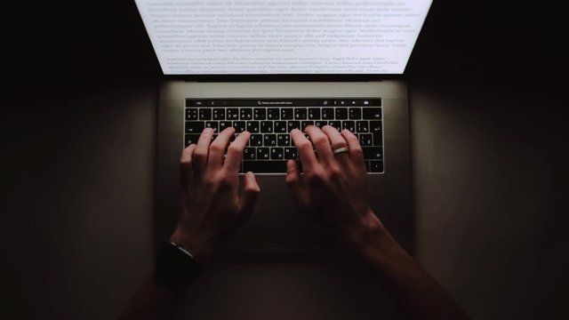 Man is working typing use laptop computer at home office at dark night. Writer flat lay top view workplace