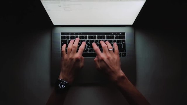 Man is working typing use laptop computer at home office at dark. Writer flat lay top view workplace