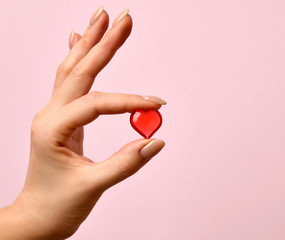 Woman hand hold little red heart on pink 