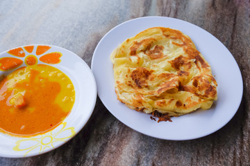 Roti canai and curry sauce on the plate over dining table