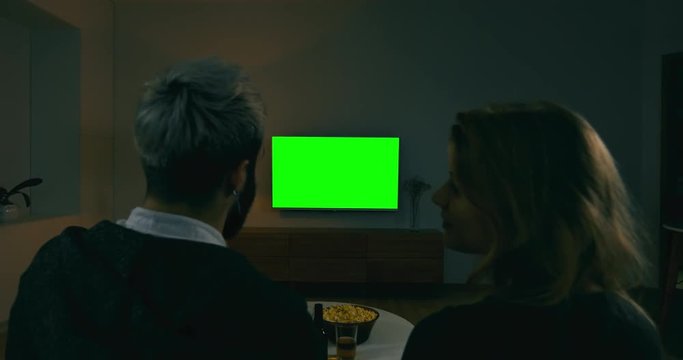 GREEN SCREEN Back view of young adult Caucasian couple sit on couch at home, watching TV. 4K UHD
