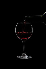 Glass of a red wine is pouring wine from a bottle of red .