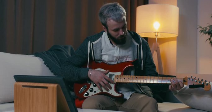 Young Caucasian male learns to play guitar through online course. Modern education concept. 4K UHD