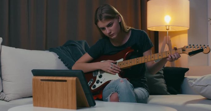 Young Caucasian female learns to play guitar through online course. Modern education concept. 4K UHD