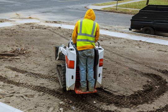 A small excavator works on the street in the summer