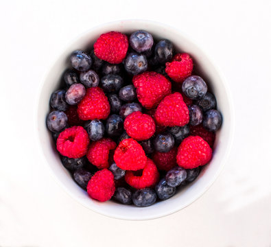 White Ceramic Bowl Full of Bluberries and Red Raspberries on a white background