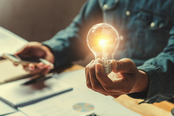 concept idea saving energy. businessman hand holding lightbulb in office