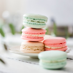 Colorful French or Italian macarons stack on white plate put on wood table with copy space for background. Dessert for served with afternoon tea or coffee break. Beautiful meal background with blank.