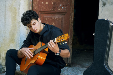 Young man playing guitar in the yard . Street musician