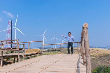 The man with viewpoint at wind turbine construction in field and meadow on the mountain with the beautiful sky cloud background at Khao Kho district, Phetchaboon province, Thailand.