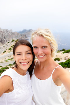 Girlfriends taking selfie photo with phone. Two beautiful young women best friends self-portrait picture on summer vacation. Multiracial asian brunette woman, blonde woman on Europe Spain travel trip.