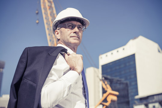 Senior elegant builder man in suit at construction site on sunny