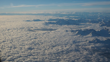 The peaks of the mountains sprout from the clouds that cover the earth. Landscape from the airplane window