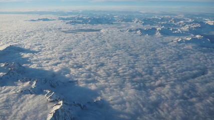 The peaks of the mountains sprout from the clouds that cover the earth. Landscape from the airplane window