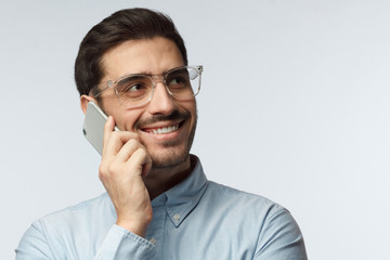 Indoor picture of young man pictured isolated on gray background holding cellphone next to ear during communication smiling with confidence