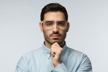 Close up portrai of suspicious man in blue shirt, trying to read your thoughts, isolated on grey...