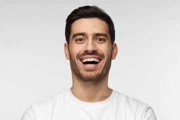 Close up horizontal shot of handsome unshaven young man in white tshirt laughing out loud, smiling broadly