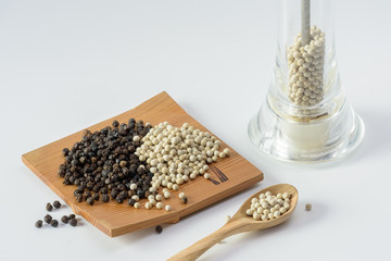 seeds of white pepper on spoon with white and black pepper seeds on white background