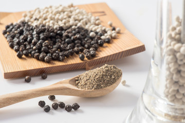 powderof black pepper on spoon with white and black pepper seeds on white background