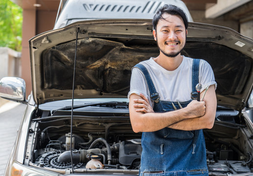 Fixing car engine in automobile repair garage. Handsome mechanics in uniform are repairing car while working in auto service