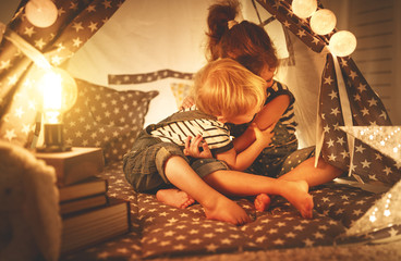 happy family children brother and sister play, laugh and hug   in dark tent in playroom