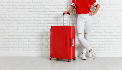 concept travel and tourism. legs of  girl with a red suitcase near white empty brick wall