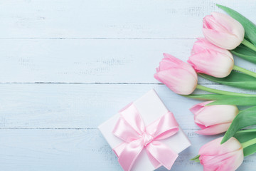 Gift or present box and pink tulip flowers on blue wooden table top view. Greeting card for Womans or Mothers Day. Flat lay.