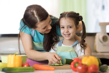 Woman and kid girl preparing a vegetables salad in the kitchen