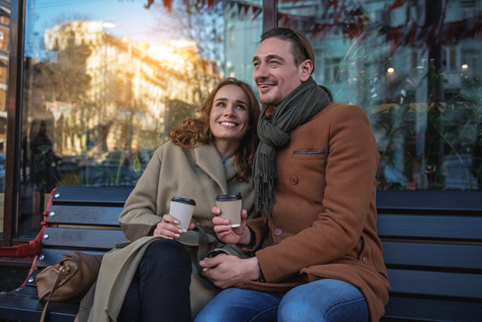 Portrait of relaxed young loving couple enjoying coffee outside. They are hugging and smiling