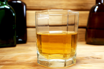 Glass of whiskey and bottles on a wooden background.