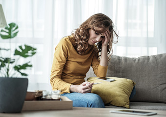 Worried girl looking at pregnancy test stick with frustration. She is sitting on couch in living...