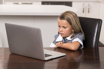 little girl 6 to 8 years old sitting at home kitchen enjoying with laptop computer concentrated watching internet cartoon movie