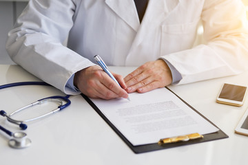 Close up of male doctor sitting at desk and writing notes on clipboard