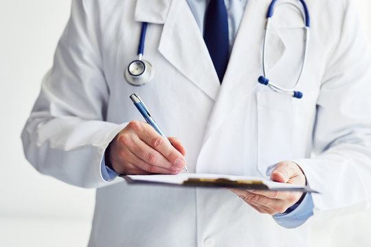 Male doctor writes notes on clipboard in office