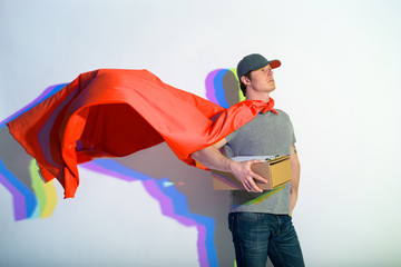 Portrait of proud courier keeping package while wearing red cape. Honor and delivery concept