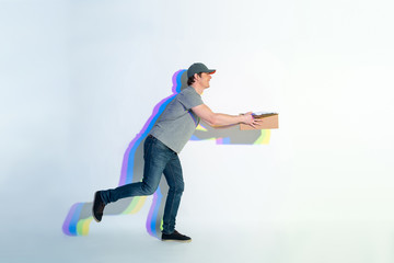 Full length side view laughing courier running with carton box. Multicolored shadow situating on wall. Conveyance concept