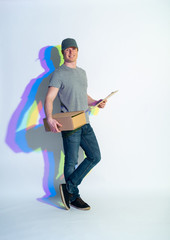 Full length portrait of cheerful male keeping parcel and document in arms. Painted reflection. Conveyance concept