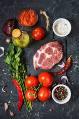 Raw marbled meat steak with ingredients for cooking on dark stone background